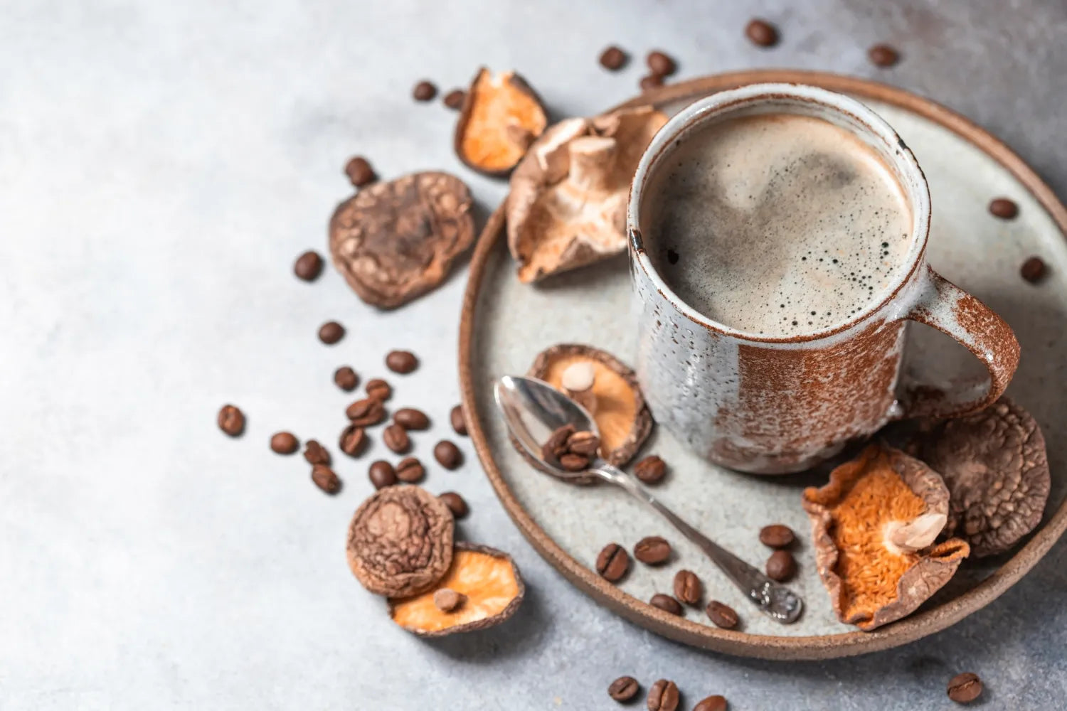 Mug of mushroom coffee on a ceramic plate with scattered coffee beans and dried mushroom pieces on a gray tabletop