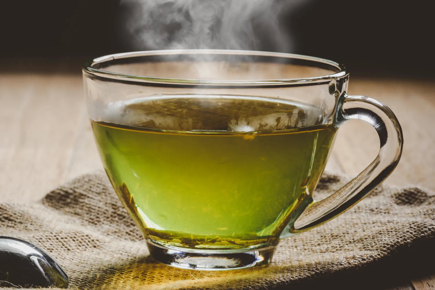 Steaming glass cup of green tea on a burlap cloth on a wooden table