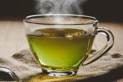 Steaming glass cup of green tea on a burlap cloth on a wooden table
