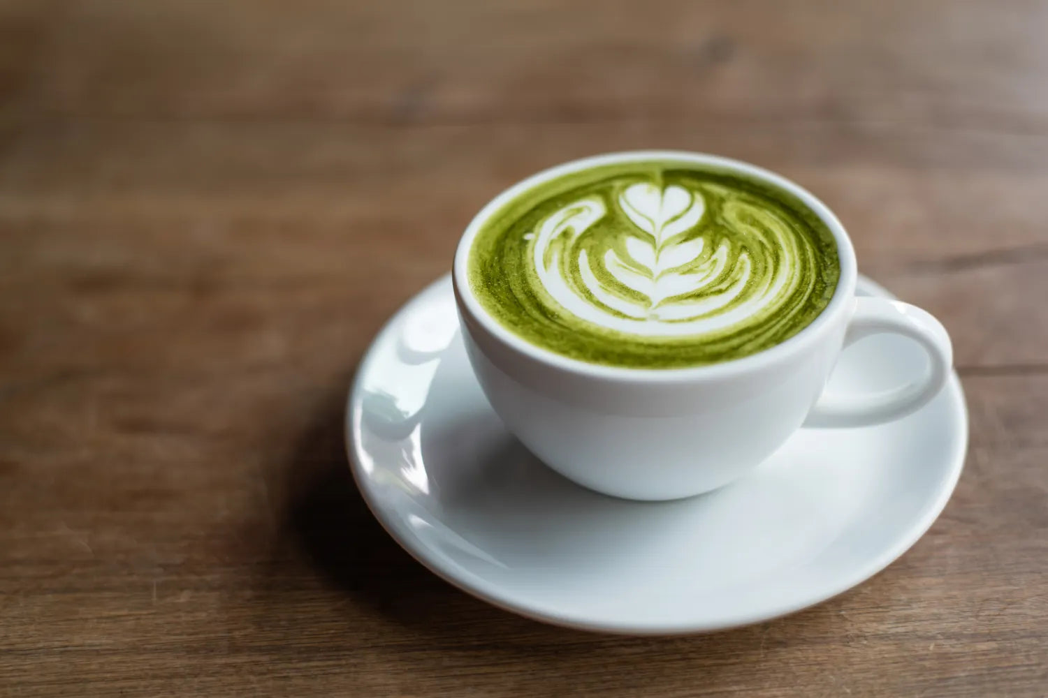 High-angle view of matcha latte in white cup and saucer showcasing leaf latte art on a wooden table