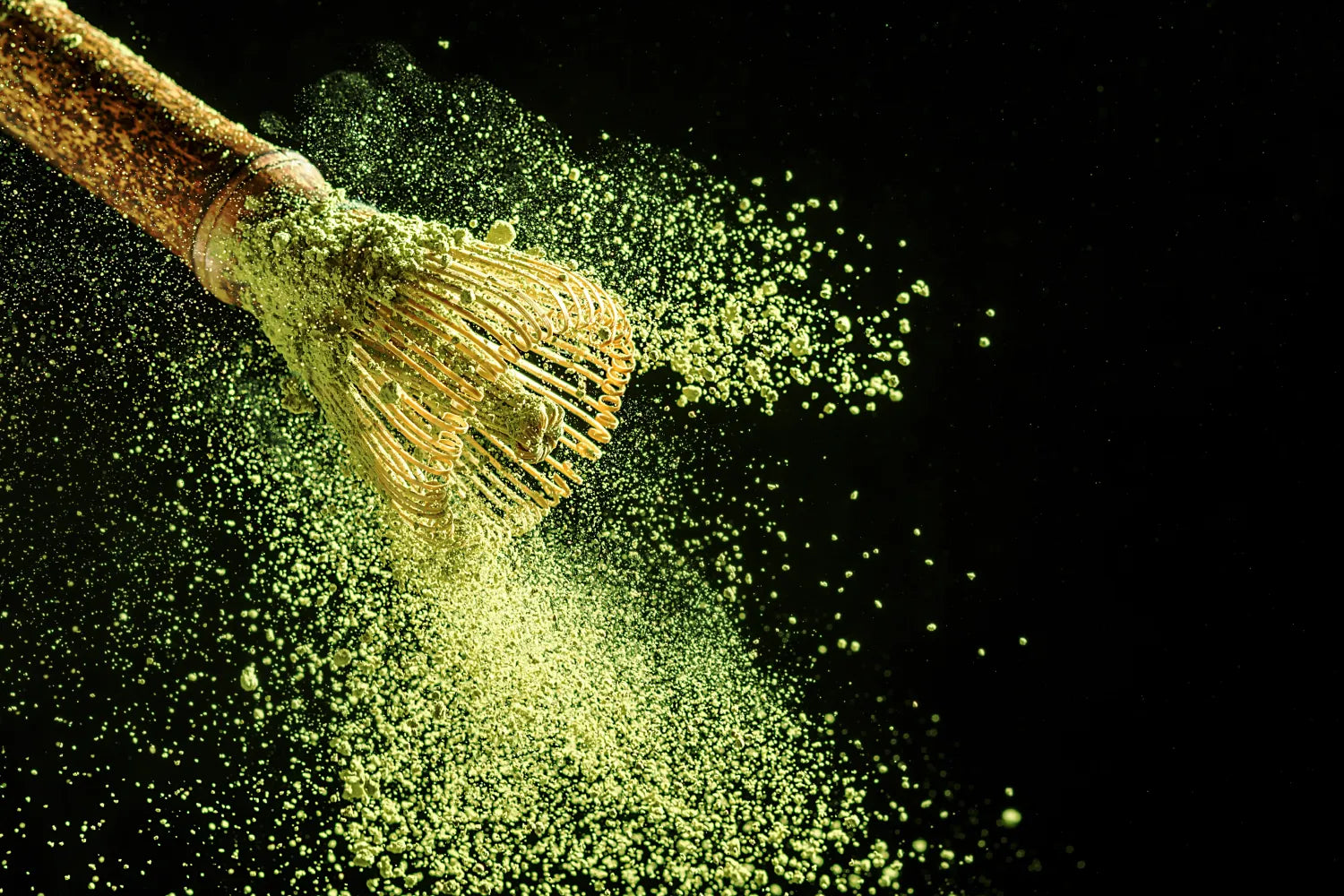 Bamboo matcha whisk scattering bright green matcha powder against a black background