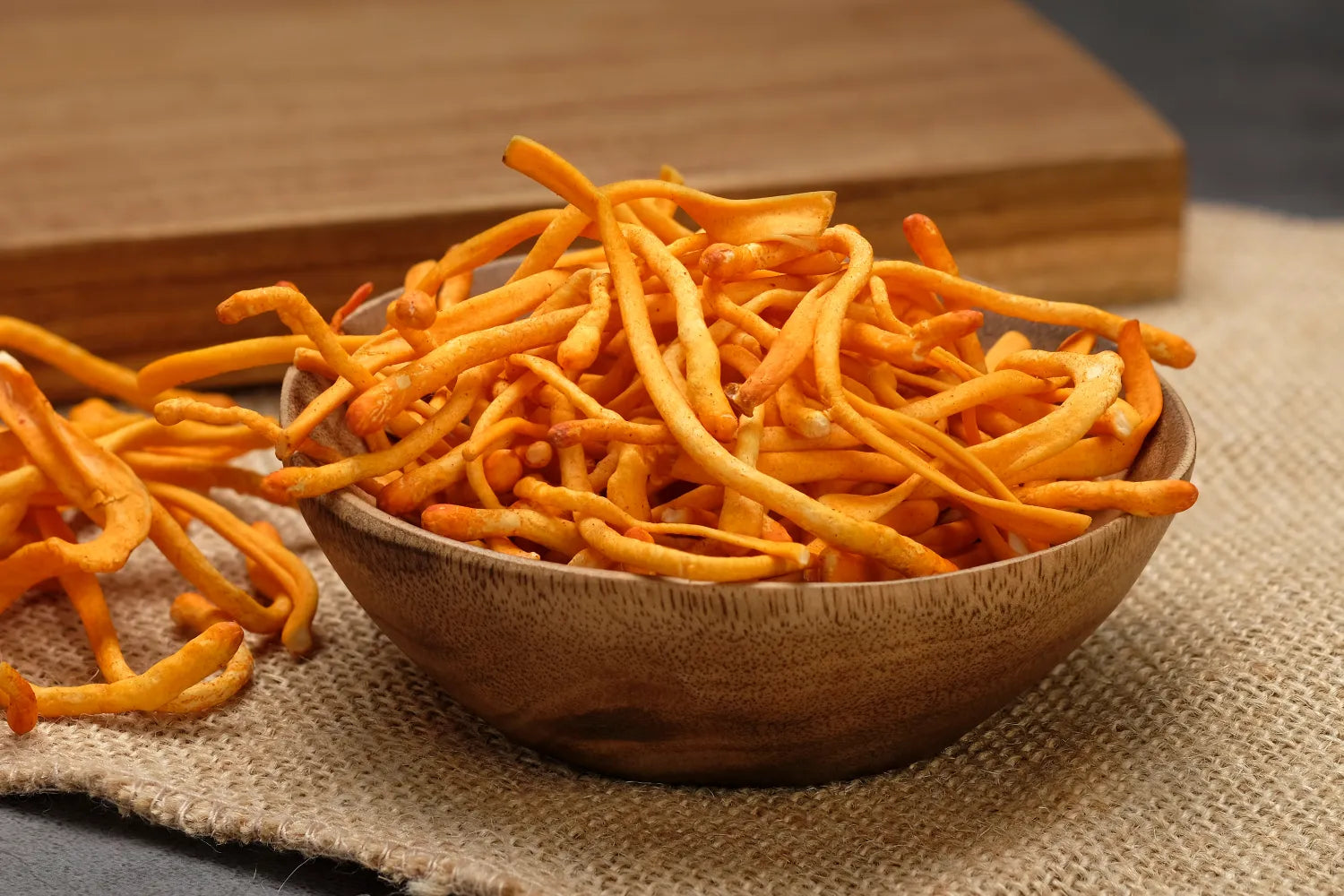 Close-up of dried cordyceps mushrooms in a wooden bowl showcasing thin orange strands on a burlap surface