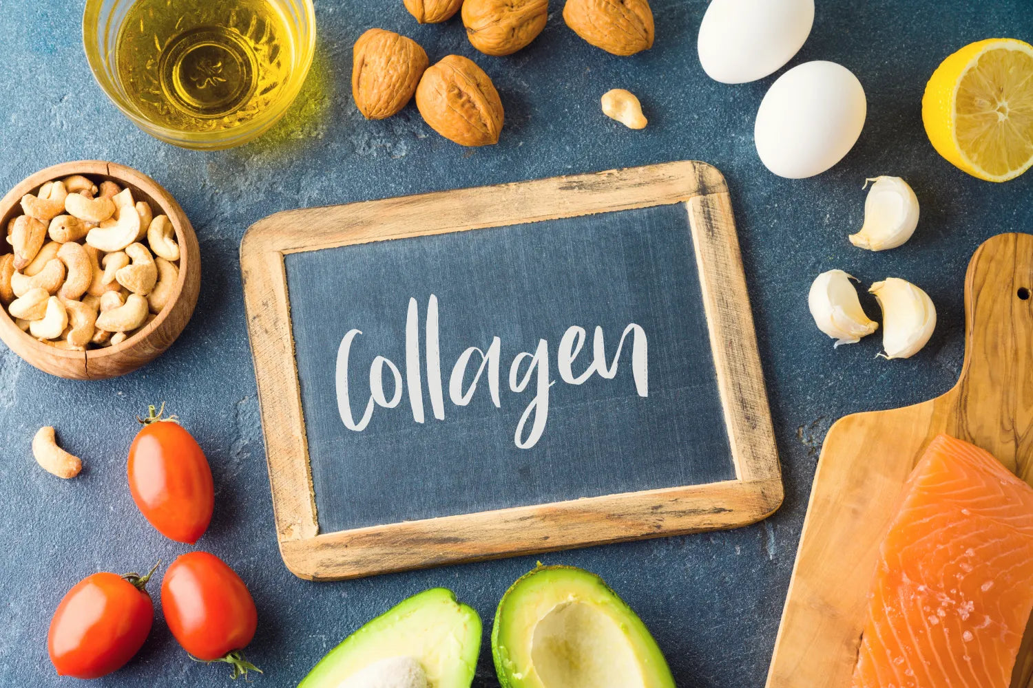 Salmon, avocado, tomatoes, nuts, eggs, garlic and lemon arranged around a chalkboard that reads Collagen