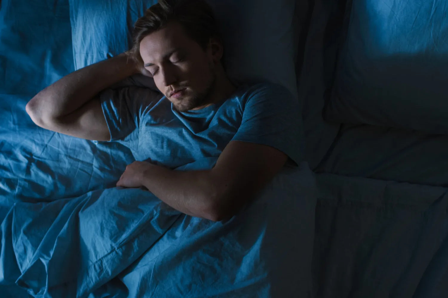Man sleeping in bed at night under dim blue lighting