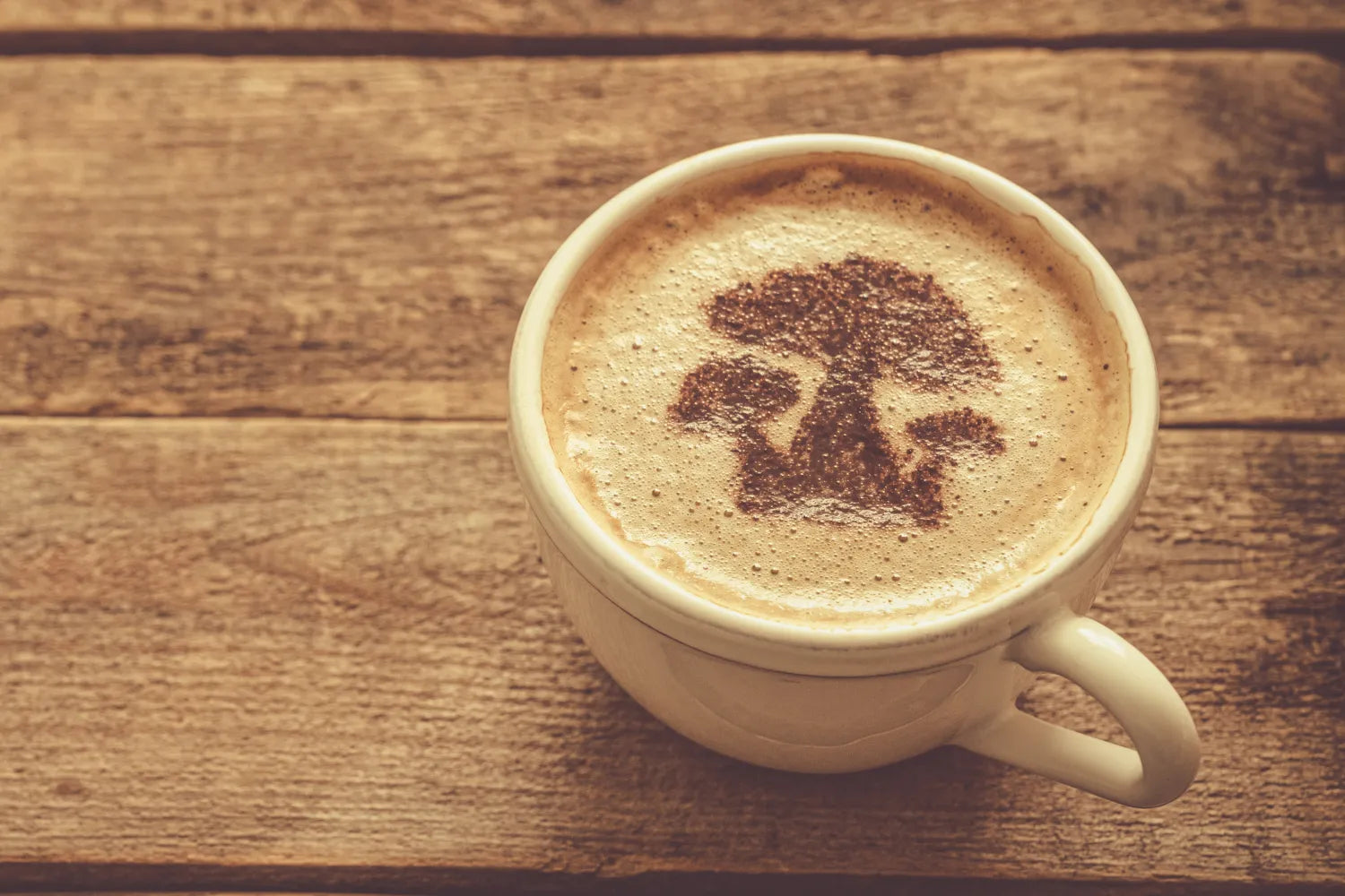 Cup of mushroom coffee with mushroom-shaped cocoa art on frothy surface, on a rustic wooden table