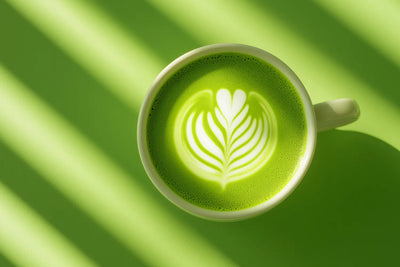Top-down view of a vibrant green matcha latte with white leaf latte art in a white mug on a green background with diagonal shadows