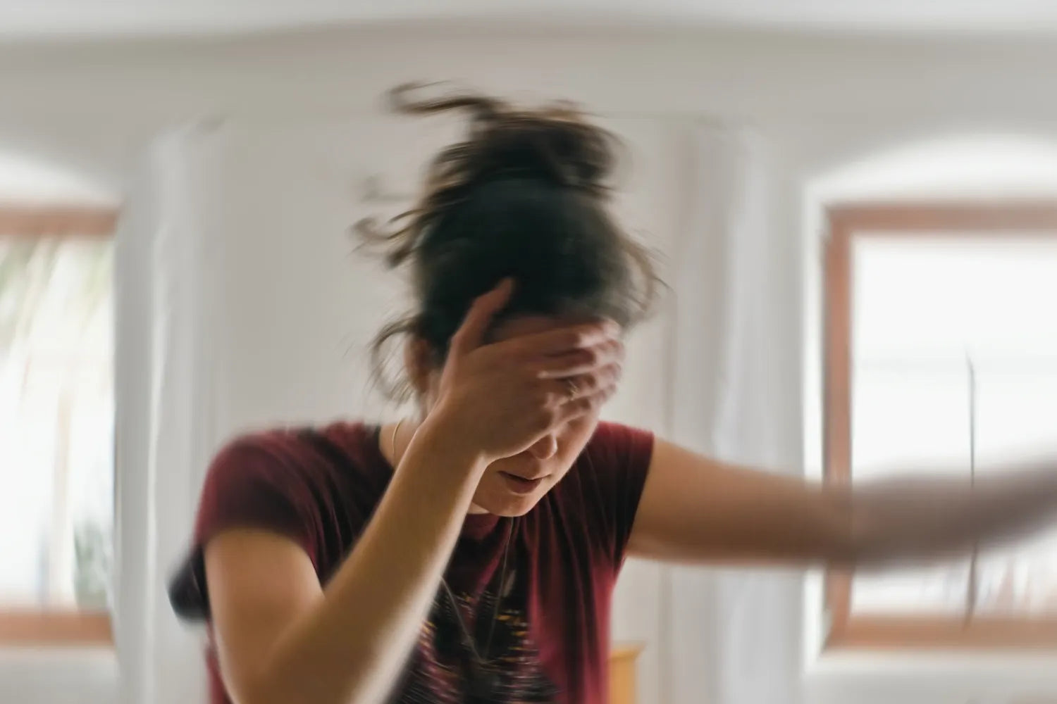 Young woman holding her forehead and appearing dizzy in a bright home interior