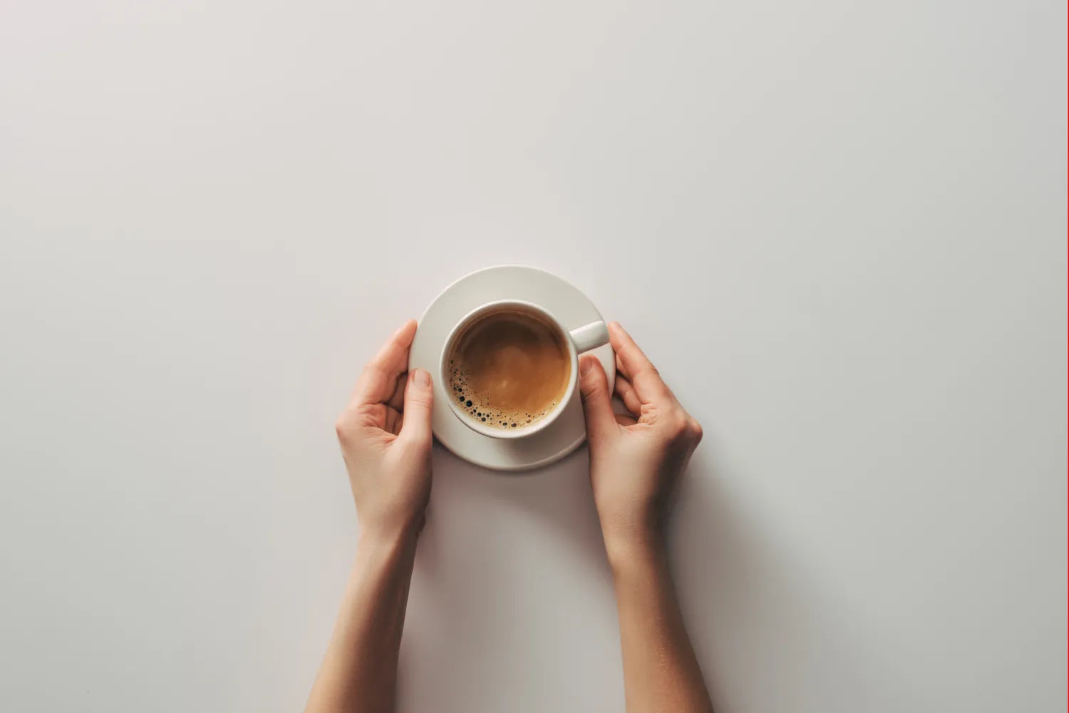 Hands holding a white cup of coffee on a plain light-gray tabletop