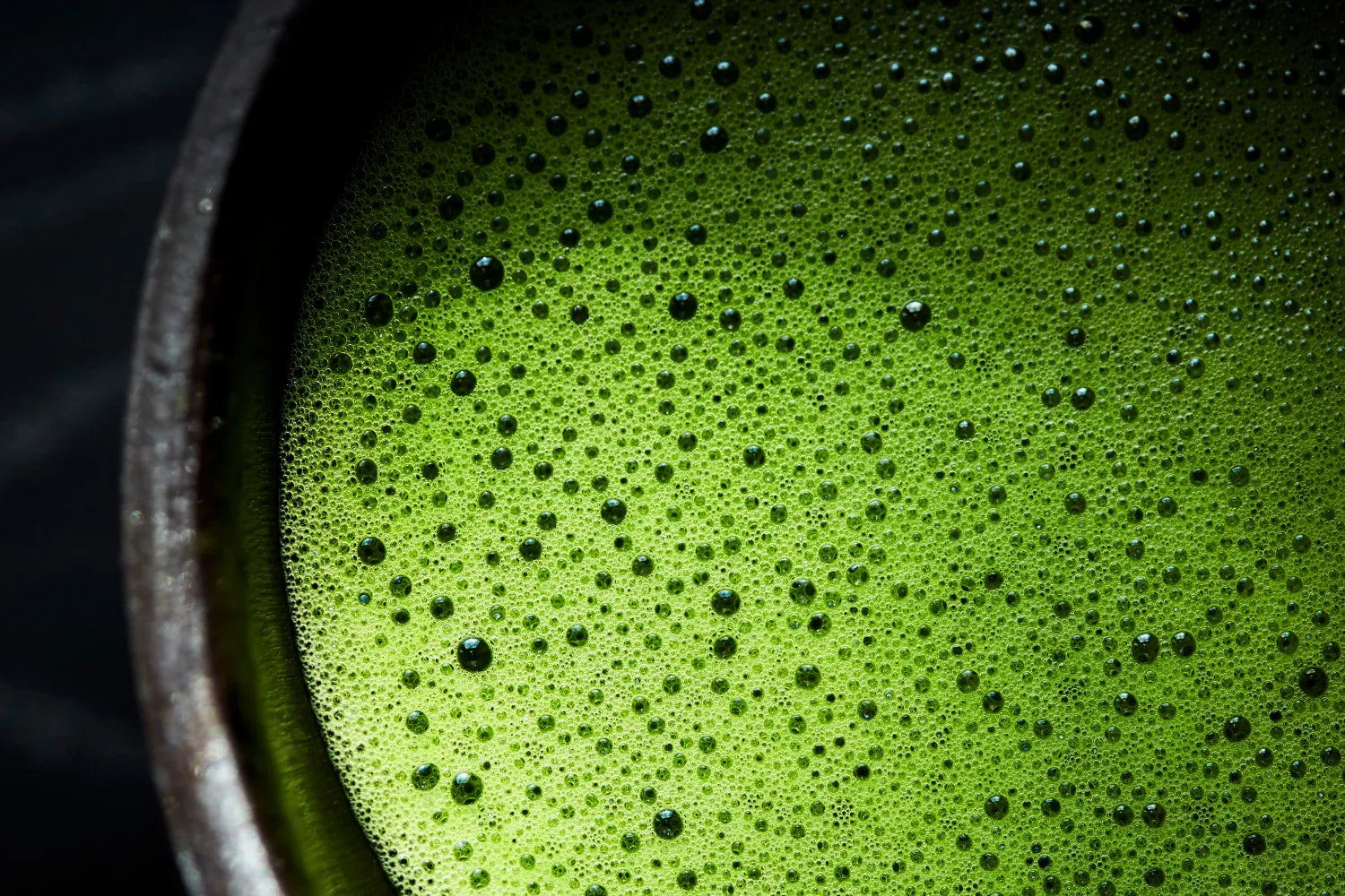 Close-up of frothy bright green matcha tea in a ceramic bowl showing dense foam and small bubbles