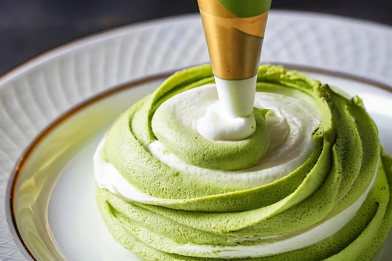 Close-up of matcha whipped cream being piped into a green-and-white swirl, showing alternating matcha and cream layers on a white plate