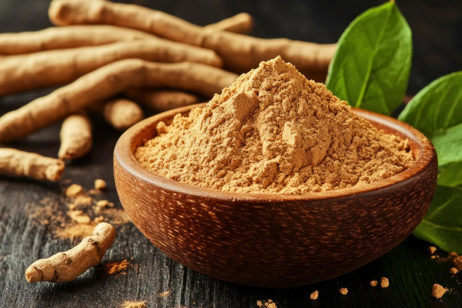 Close-up of ashwagandha powder in a wooden bowl showing fine tan powder with roots and green leaves on dark wood