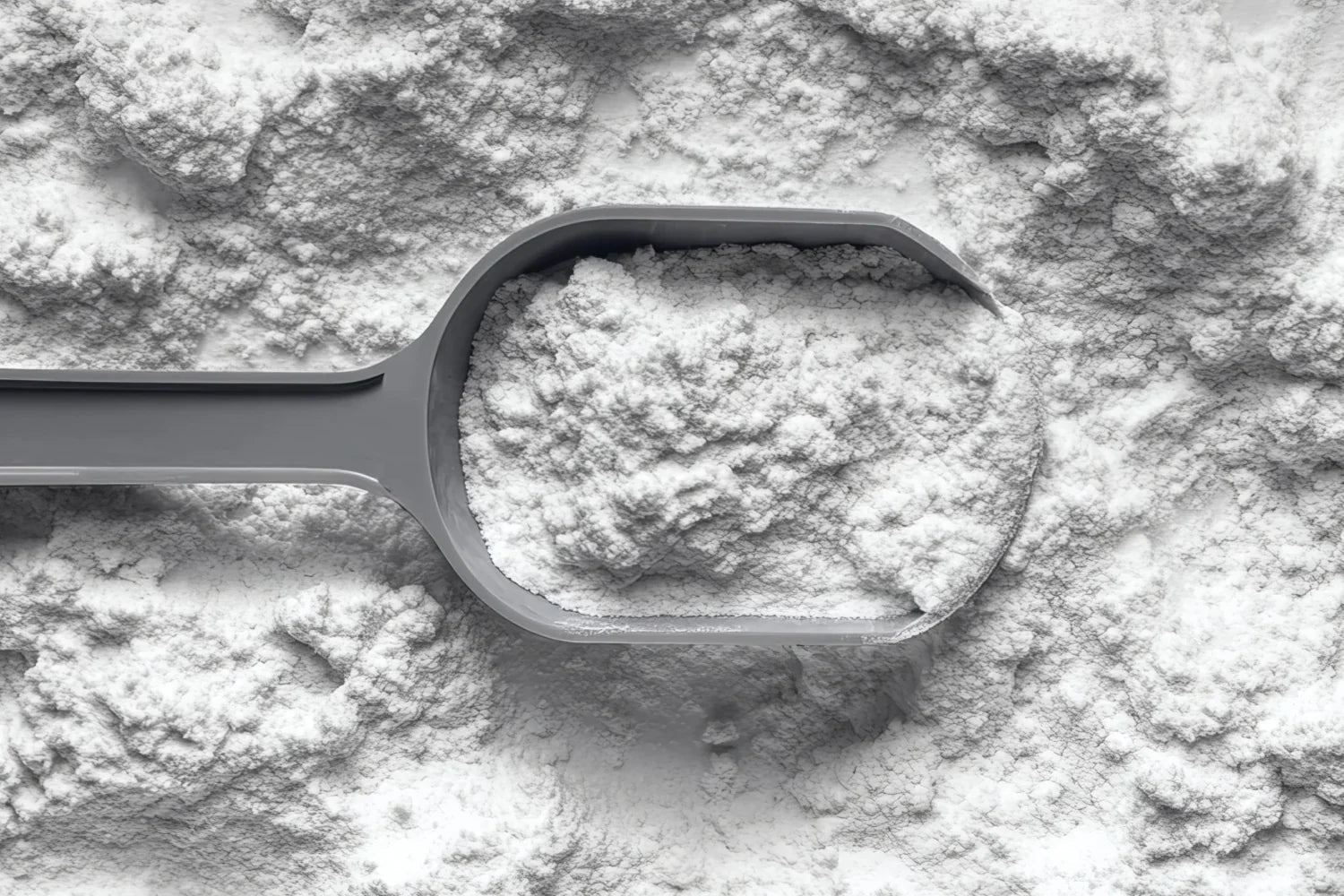Top-down view of a plastic scoop filled with white supplement powder resting on a spread of loose powder