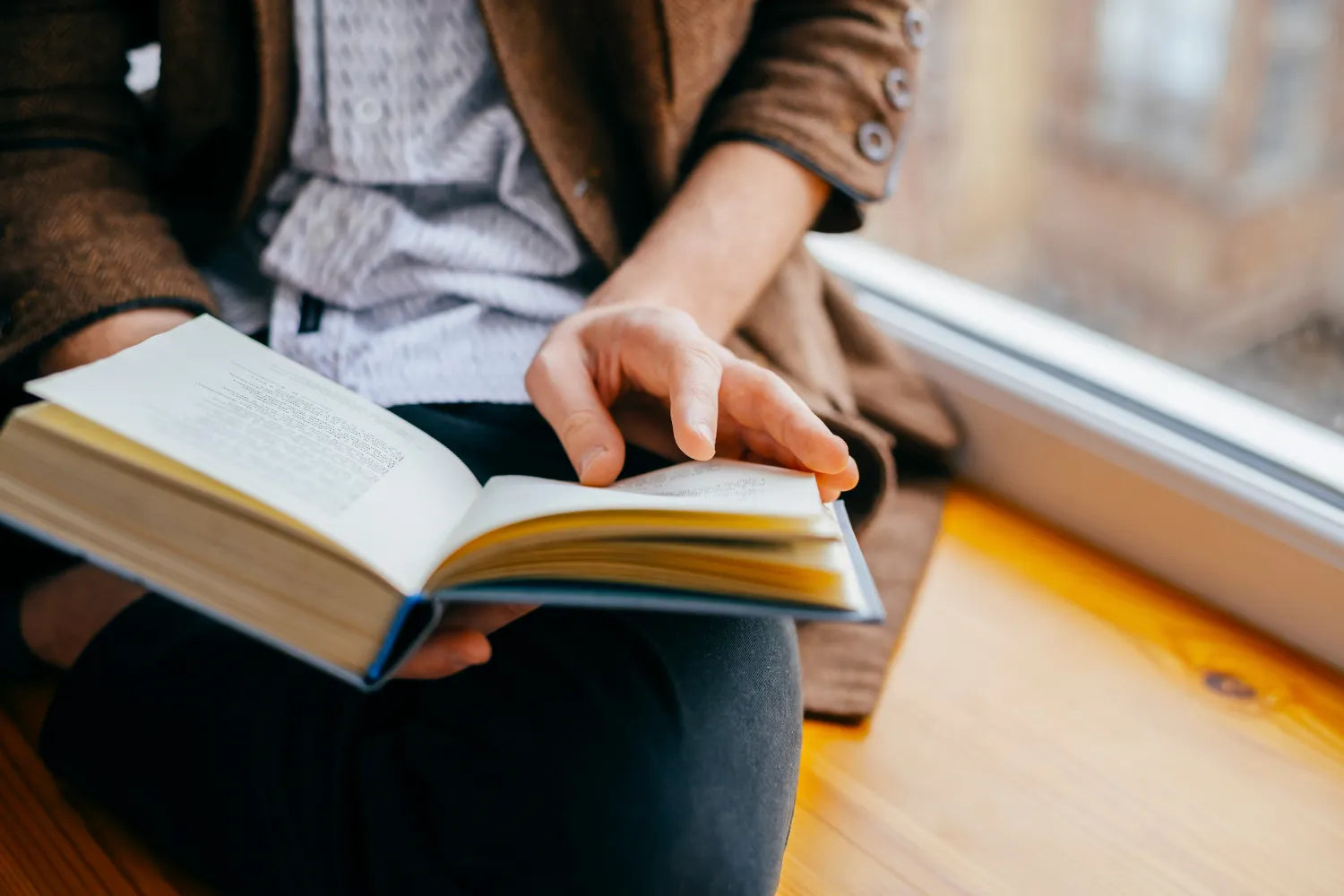 Person turning a page while reading a paperback book on a windowsill