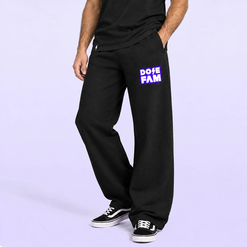 Model wearing black wide leg sweatpants with a purple and white DOPE FAM logo and black sneakers against a lavender backdrop