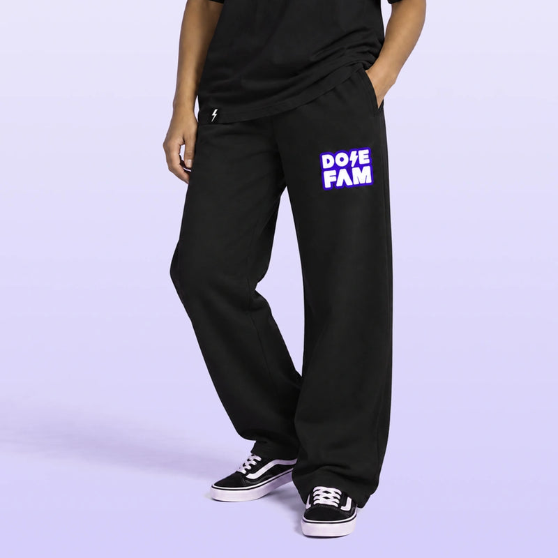 Model wearing black relaxed fit sweatpants with a purple and white DOPE FAM logo and black sneakers against a lavender backdrop