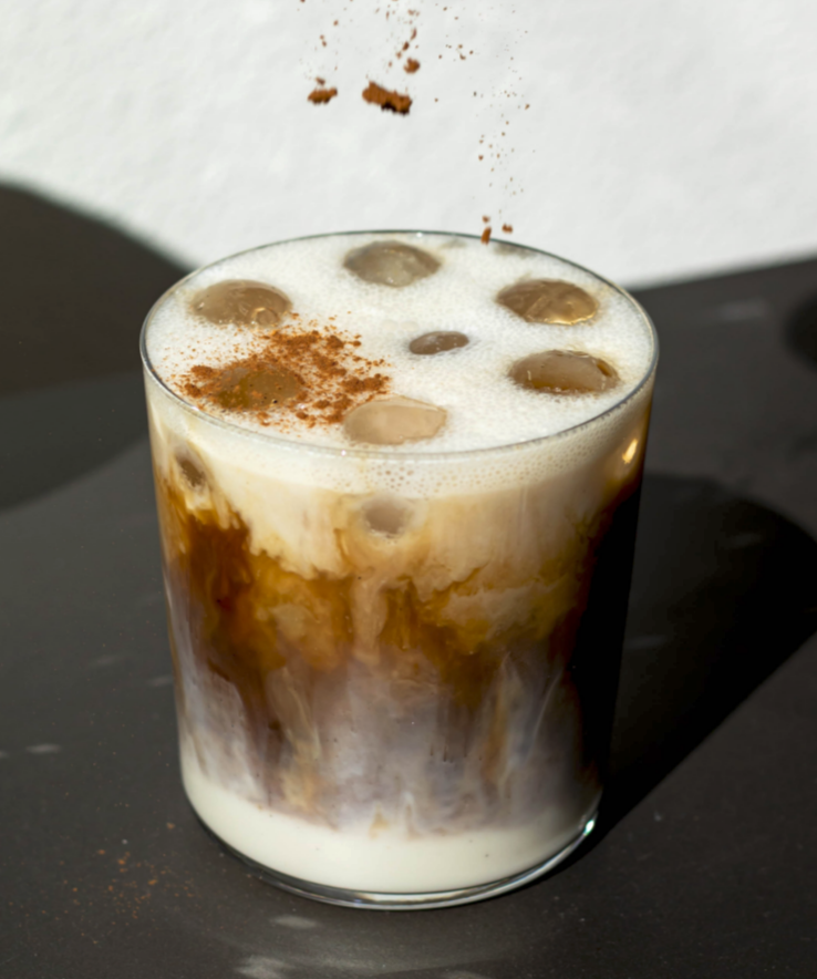 Glass of iced coffee with cream and cinnamon on a dark surface