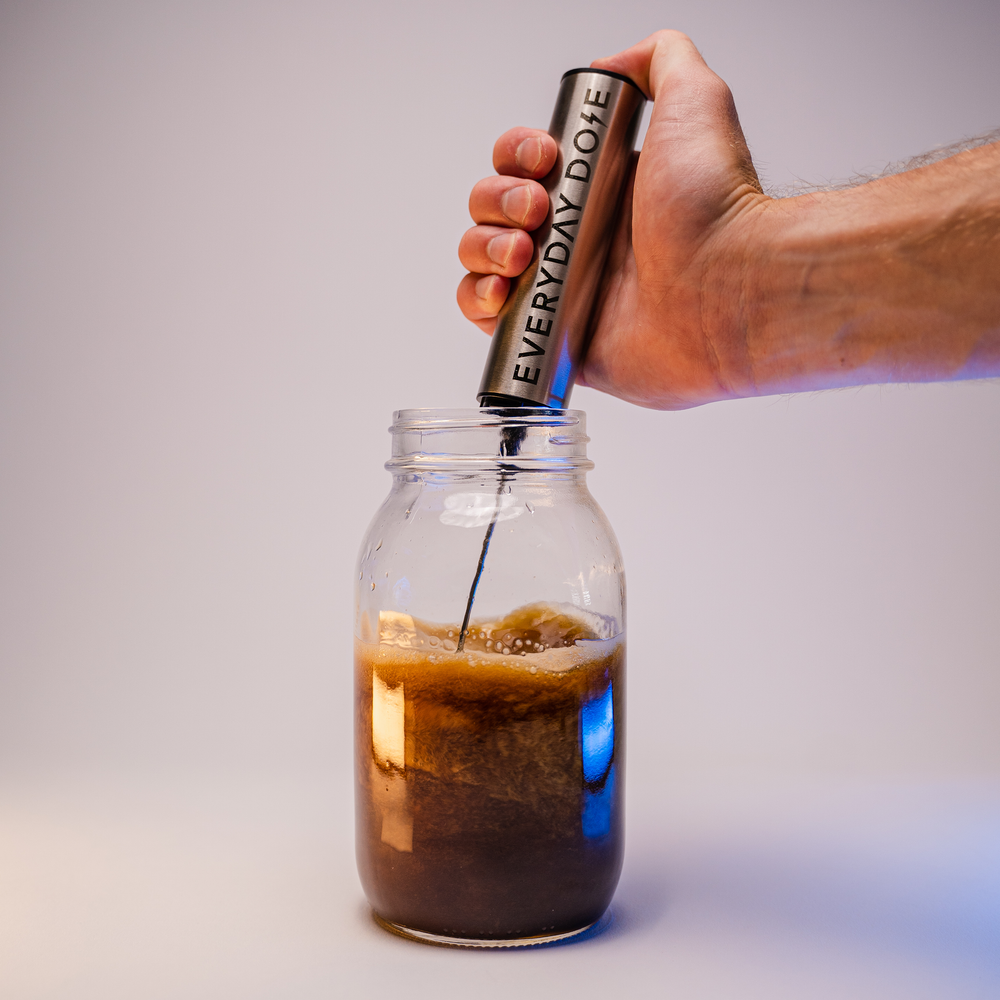 Hand using Fancy Frother to blend creamy coffee drink in glass mason jar with rich foam forming