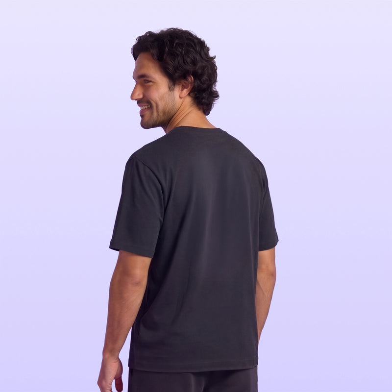 Smiling man in a black short sleeve T shirt shown from the back against a soft lavender background