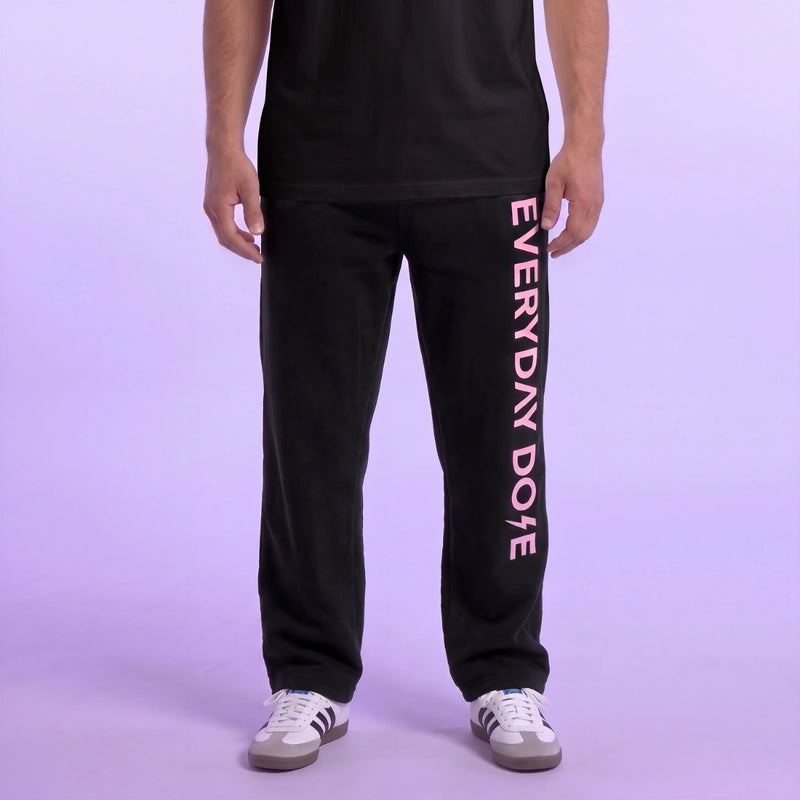 Model wearing black jogger pants with vertical pink lettering and white sneakers against a soft lavender background