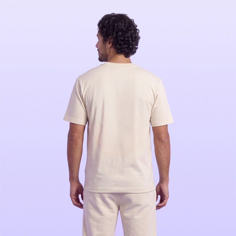 Back view of a man wearing a cream short sleeve T shirt and matching pants against a soft lavender background