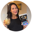 Woman smiling holding a glass of everydaydose coffee in one hand, a bag of everydaydose powder in the other 