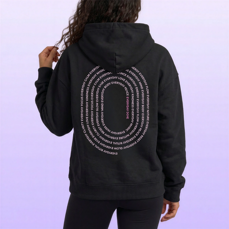 Model wearing a black hooded sweatshirt with white circular text design on the back against a pale lavender background