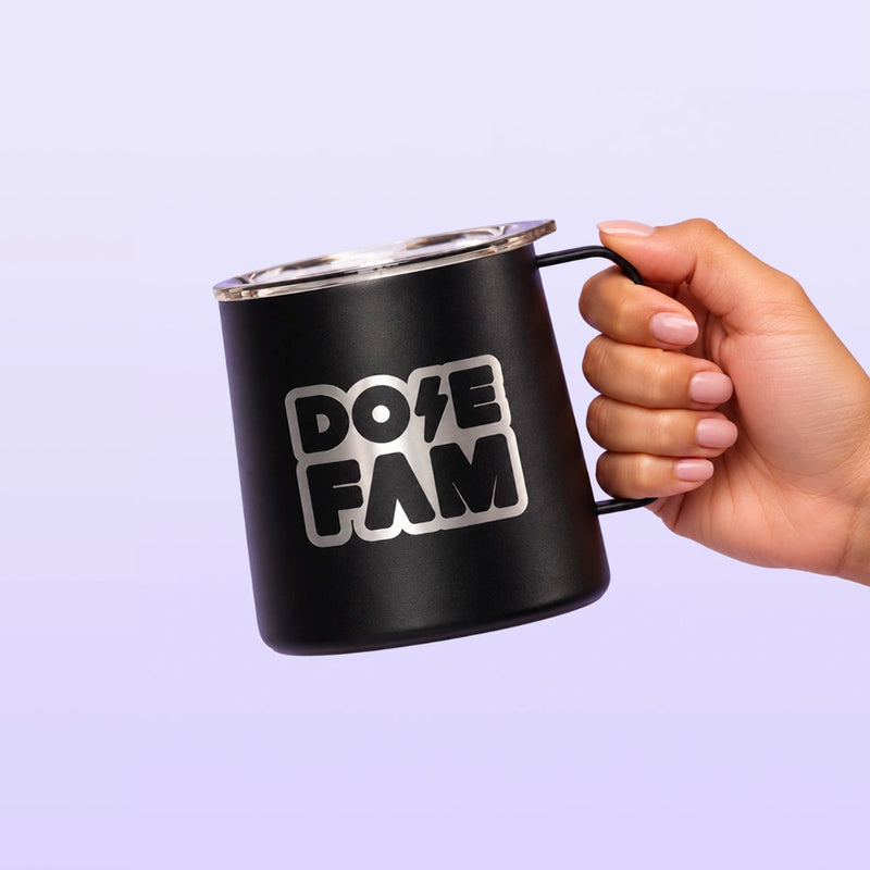 Black handled mug with a white DOPE FAM logo held by a hand against a soft lavender background