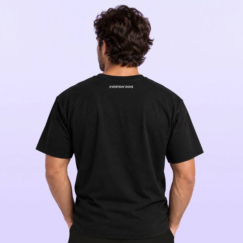 Back view of a man wearing a black T shirt with small Everyday Dope lettering at the neckline against a pale lavender background