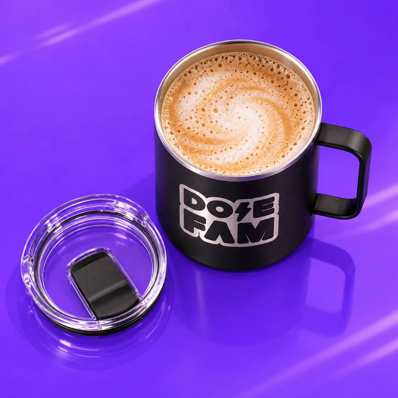 Black handled mug filled with foamy coffee and marked with a white DOPE FAM logo beside its clear lid on a vivid purple surface