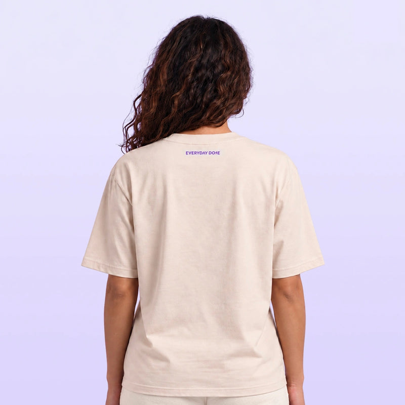 Back view of a model wearing a cream short sleeve T shirt with small purple Everyday Dope lettering against a lavender background