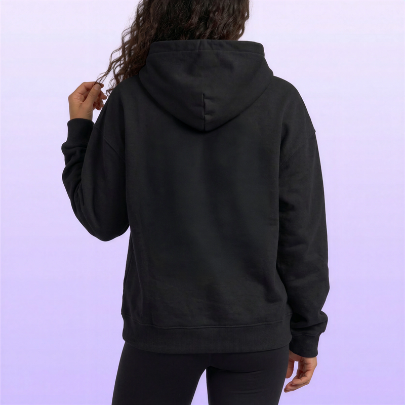 Back view of a woman wearing a plain black hooded sweatshirt with ribbed cuffs and hem against a soft lavender background