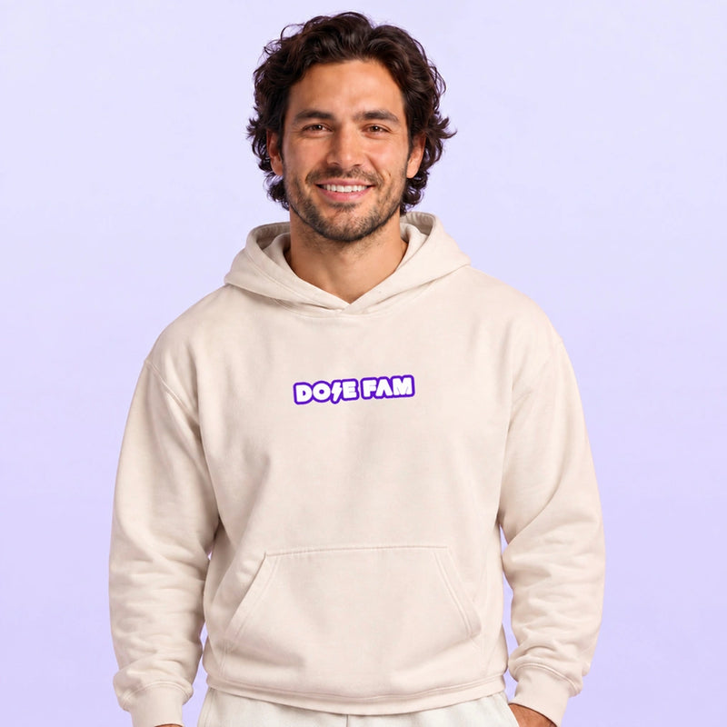 Smiling man modeling a cream pullover hoodie with a purple and white DOPE FAM chest logo against a lavender background