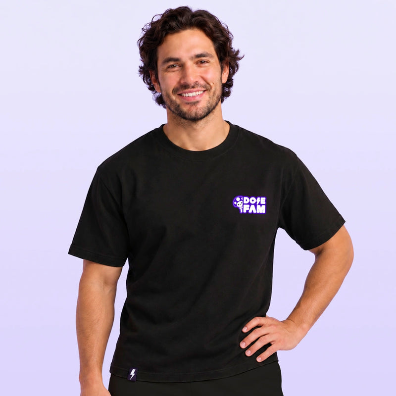 Smiling man wearing a black T shirt with a small purple and white Dose Fam logo on the chest against a lavender background