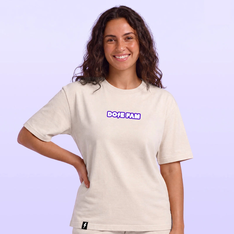 Woman modeling a cream T shirt with a purple and white Dose Fam logo against a soft lavender background