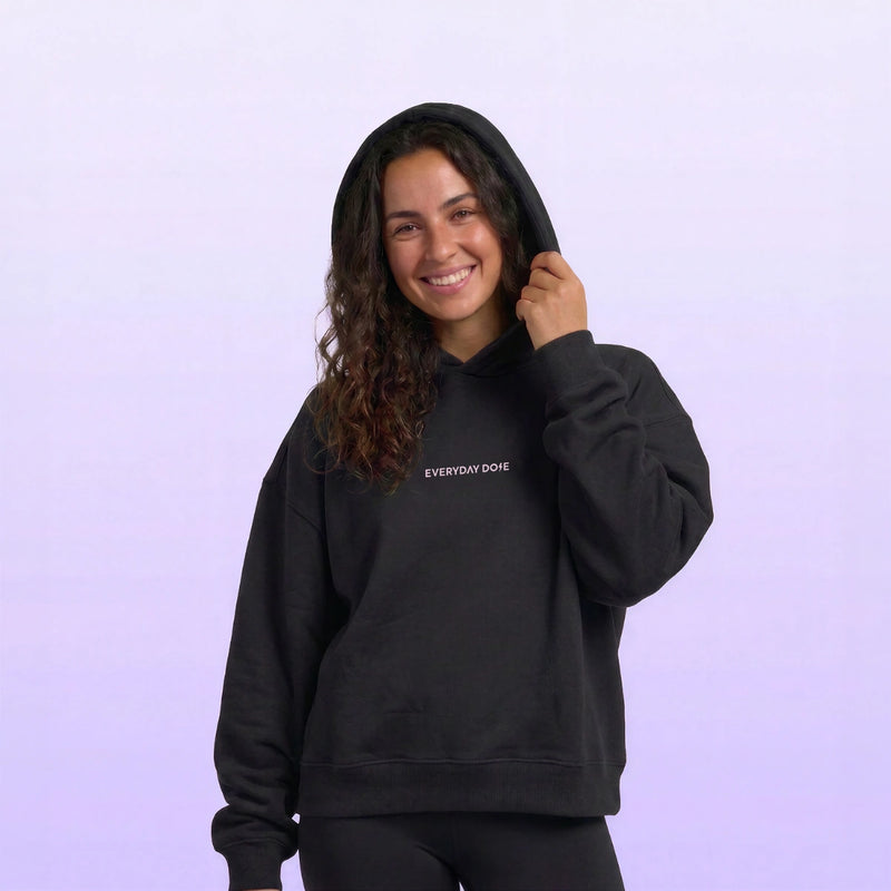 Smiling woman wearing a black hooded sweatshirt with small Everyday Dope text on the chest against a soft lavender background