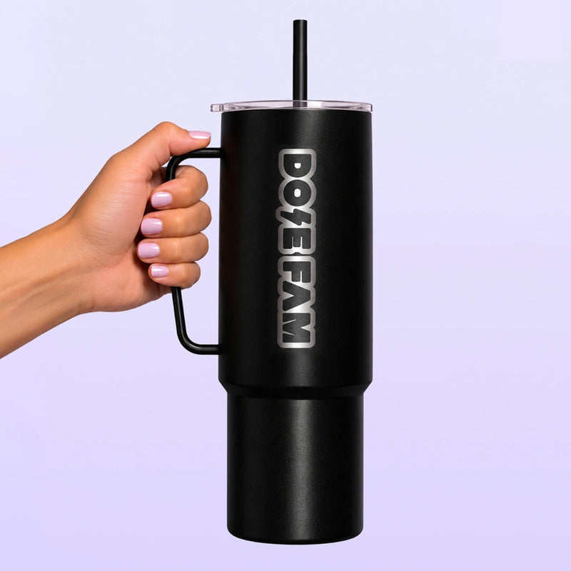 Black handled tumbler with a straw and vertical DOPE FAM logo held by a hand against a light lavender background
