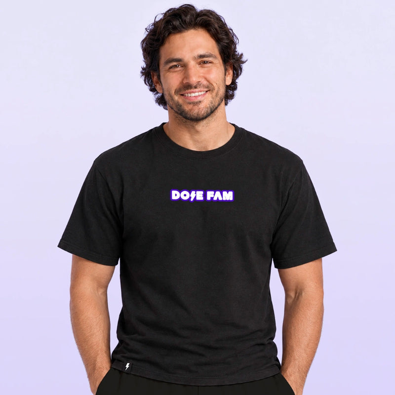 Smiling man modeling a black short sleeve T shirt with a purple and white DOSE FAM logo against a pale lavender background