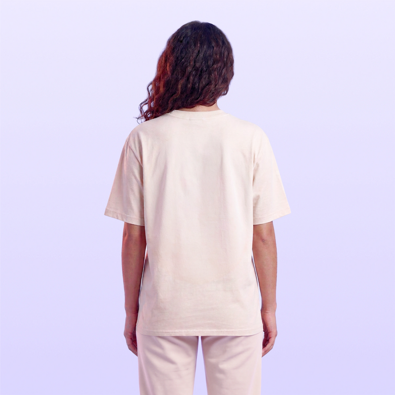Back view of a woman wearing a loose cream short sleeve T shirt and light pants against a soft lavender background