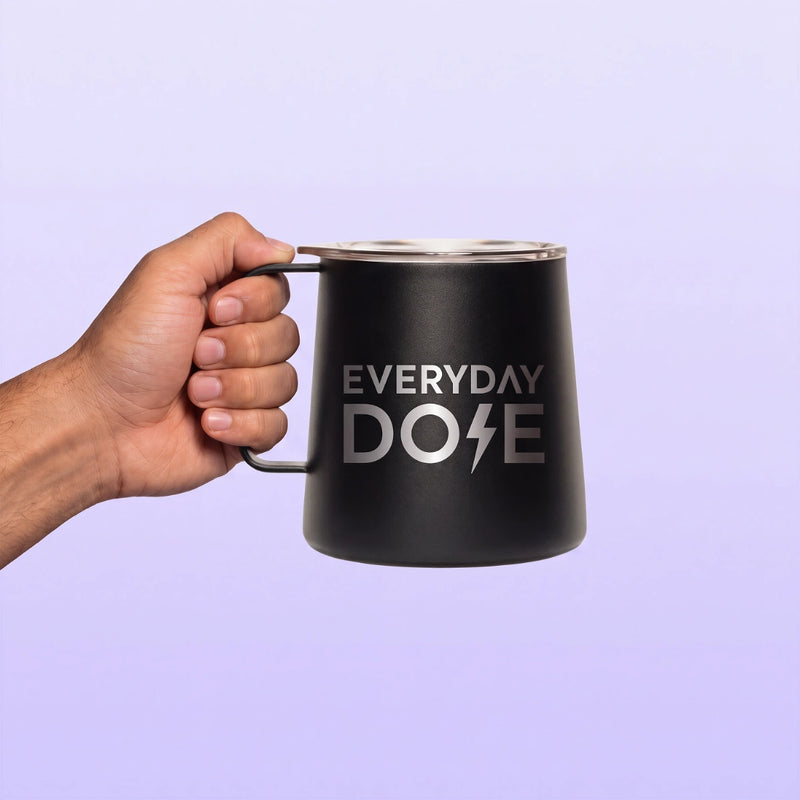 Black insulated mug with a metal rim and side handle held by a hand against a soft lavender background