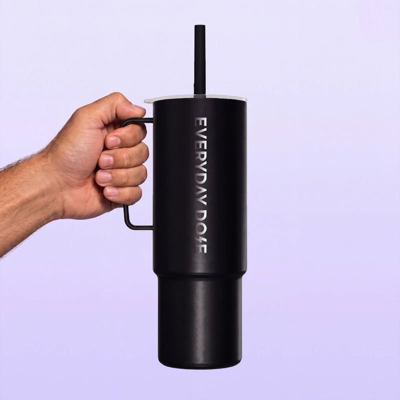 Black handled tumbler with a straw held by hand against a soft lavender background