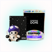 Plush mushroom toy holding coffee cup beside black notebook and bag of Everyday Dose mild roast coffee blend