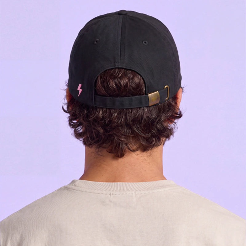 Back view of a person wearing a black adjustable cap with a pink lightning bolt detail against a pale lavender background