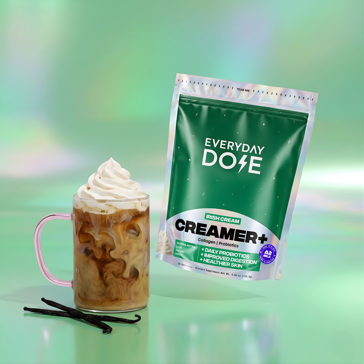Glass mug filled with iced coffee topped with whipped cream beside green resealable bag of Irish Cream creamer plus vanilla beans on green background